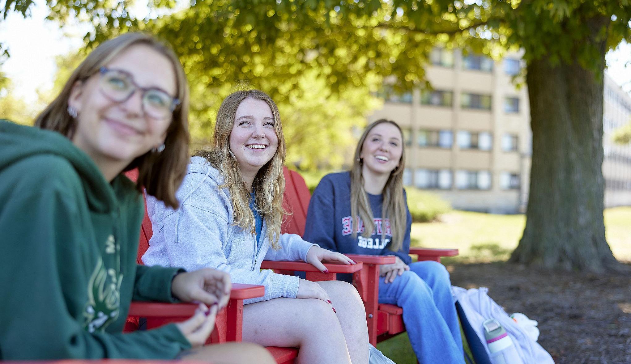 Two students unwind lakeside in Carthage's famous red adirondack chairs.